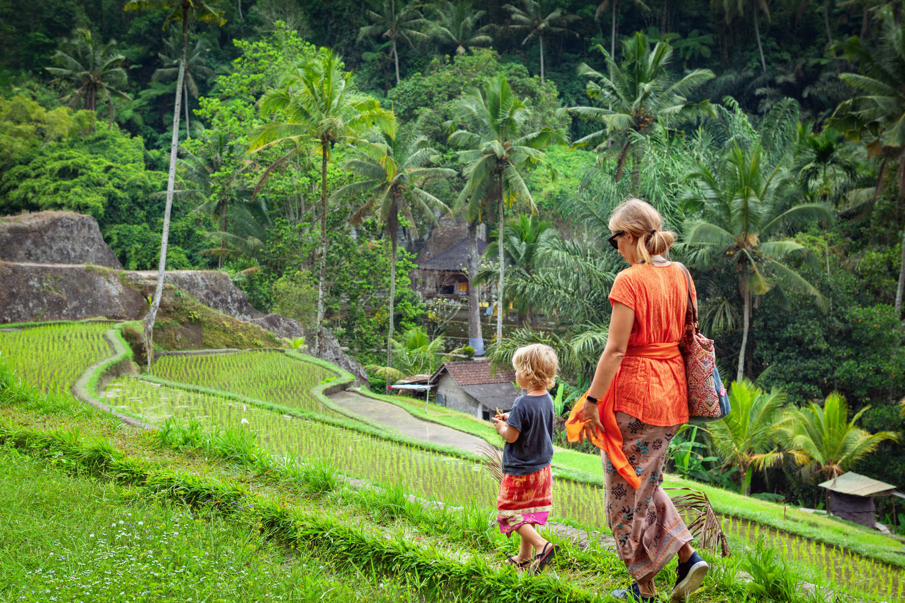 Une mère et son enfant vêtus de sarongs traditionnels marchent le long de rizières en terrasses à Bali en Indonésie