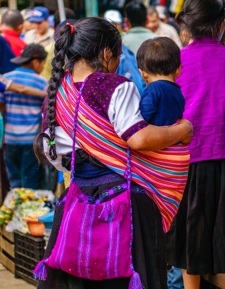 Vue de dos d'une femme portant un enfant dans un châle en tissu traditionnel aux rayures multicolores