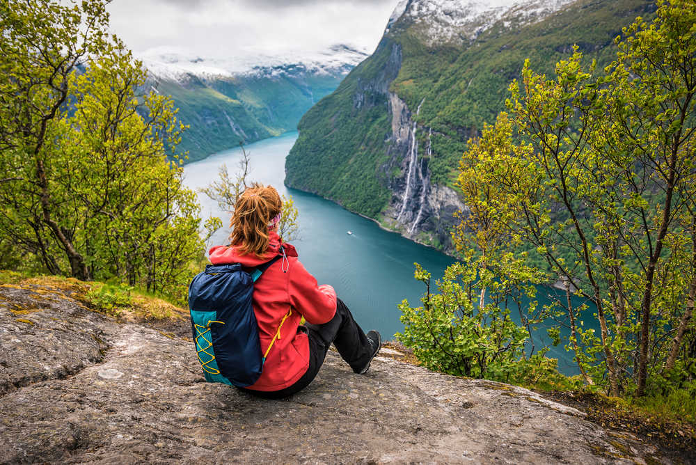 Femme avec un sac à dos assise sur un rocher au-dessus du fjord de Geiranger, Norvège