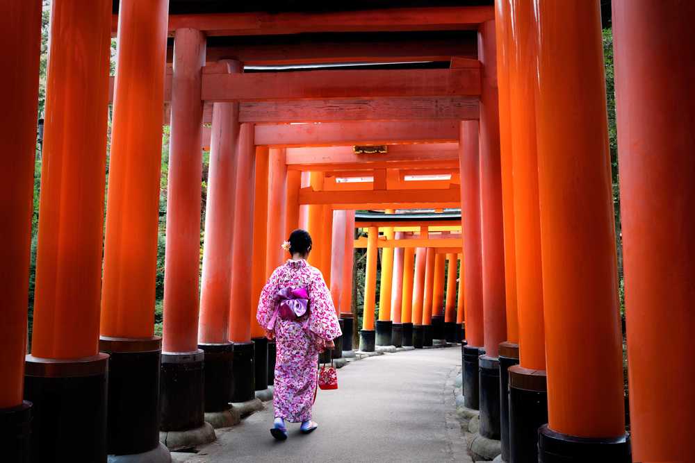 Femme habits traditionnels japonais marchant sous les portes tori au sanctuaire fushimi-inari, Kyoto Japon