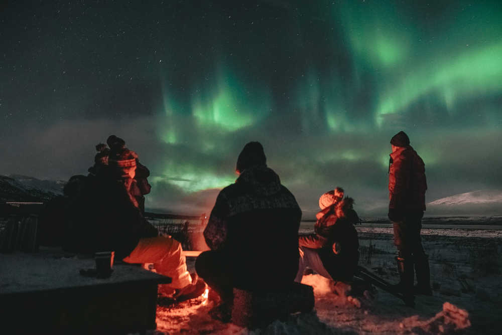 Groupe de personnes assisent autour d'un feu observant les aurores boréales, Norvège