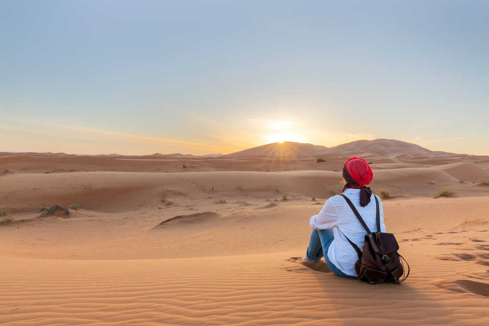 Jeune femme regardant le soleil couchant sur les dunes de Erg Chebbi de Merzouga au Maroc