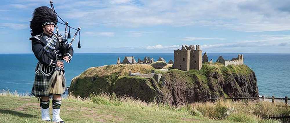 Joueur de cornemise en tenue traditionelle devant le château de Dunnottar à Stonehaven