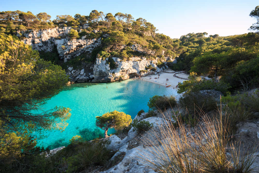 Petite crique à Minorque, la plage est entourée de montagne et l'eau est bleu turquoise