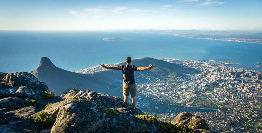 Un homme de dos fait face à la ville de Cap Town depuis les hauteurs des montagnes