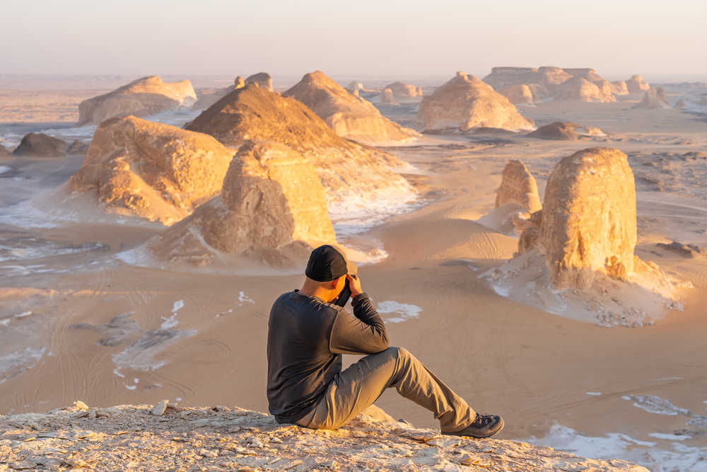 Un voyageur assis et prenant une photo du désert blanc au coucher du soleil, Basse Egypte