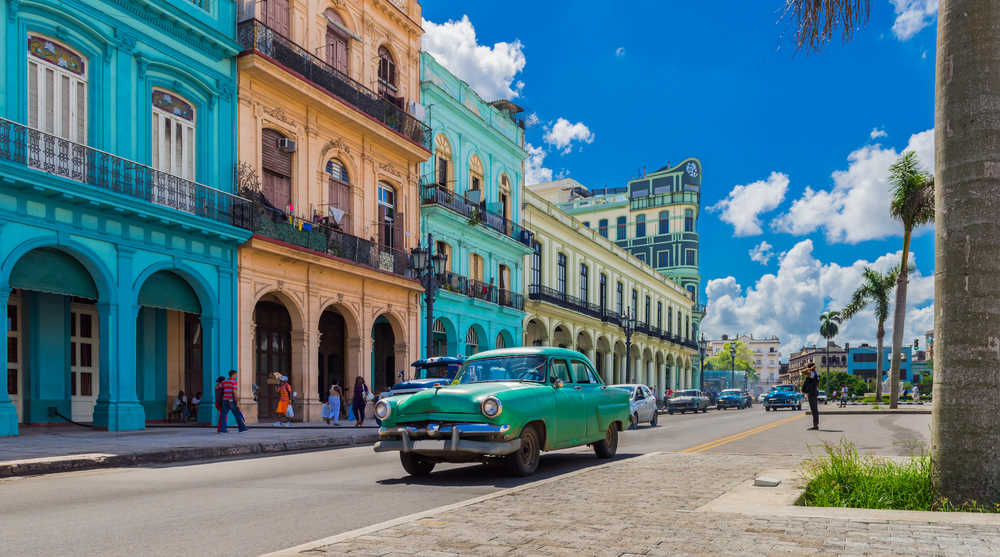 Vue sur une grande rue de la Havane, les maisons sont colorées, et une voiture verte est devant