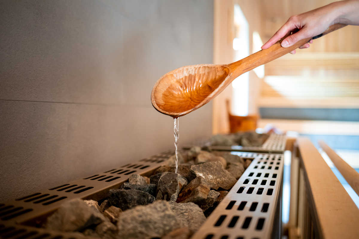 Arrosage des pierres dans un sauna finlandais © Adobe Stock Arrosage des pierres dans un sauna finlandais