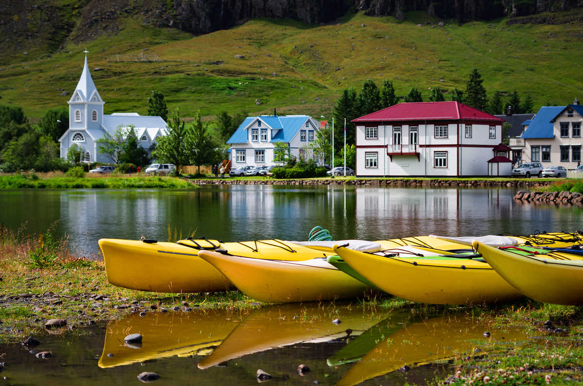 kayaks jaunes avec l'église bleue et les maisons en arrière-plan, Seydisfjordur, Islande