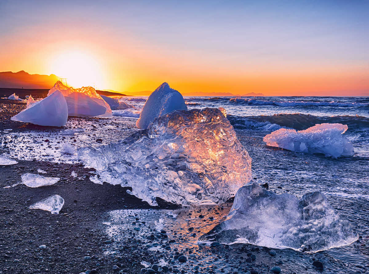 morceaux d'icebergs scintillent sur la célèbre plage de Diamond Beach, dans le lagon de Jokulsarlon, lors du coucher du soleil.