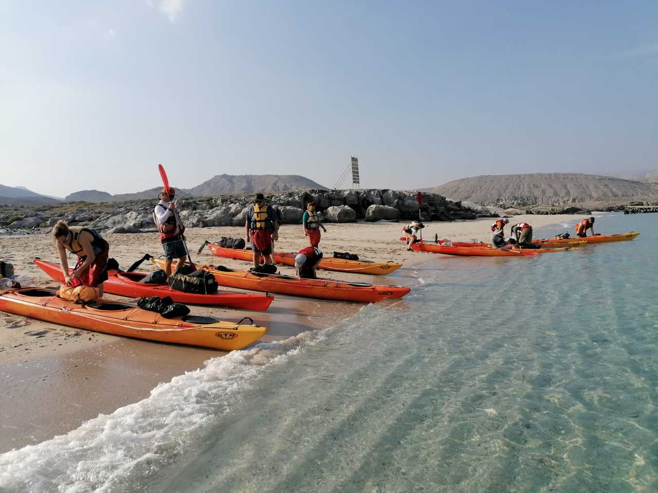 groupe de randonneurs qui se prépare à monter sur des kayaks sur une plage à Oman