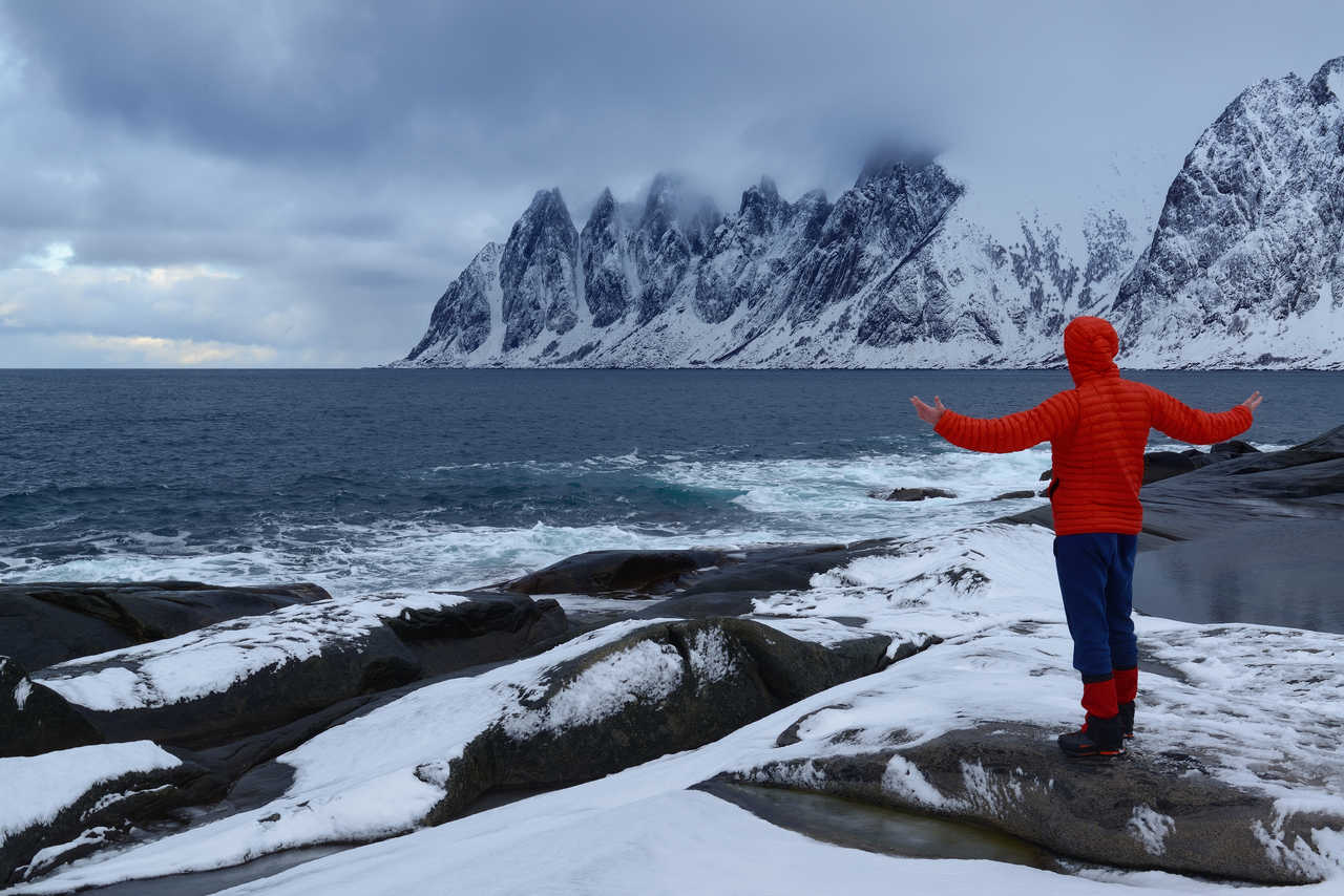 Homme au bord de l'eau, face aux paysages enneigés de l'île de Senja