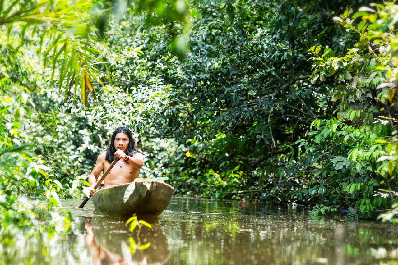Homme naviguant dans les eaux de l'Amazonie équatorienne dans un canoë traditionnel à travers la jungle primaire d'Équateur