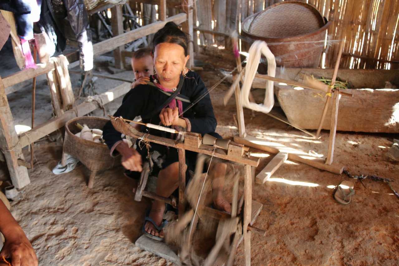 Laotienne filant la laine avec son bébé dans le dos