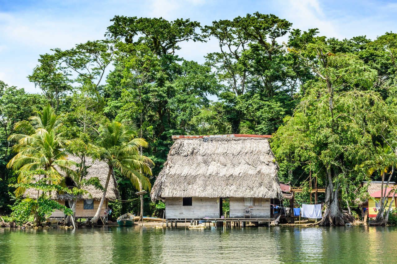 Maisons traditionnelles en bois sur pilotis avec toits en feuilles de palme séchées au bord du Rio Dulce.