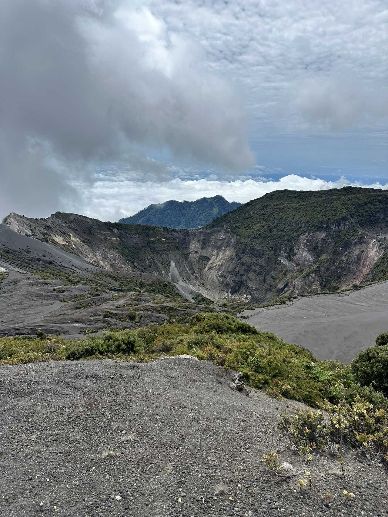 Paysage lunaire du cratère du volcan Irazú au Costa Rica, montrant des pentes de cendres volcaniques grises et une mer de nuages en altitude.