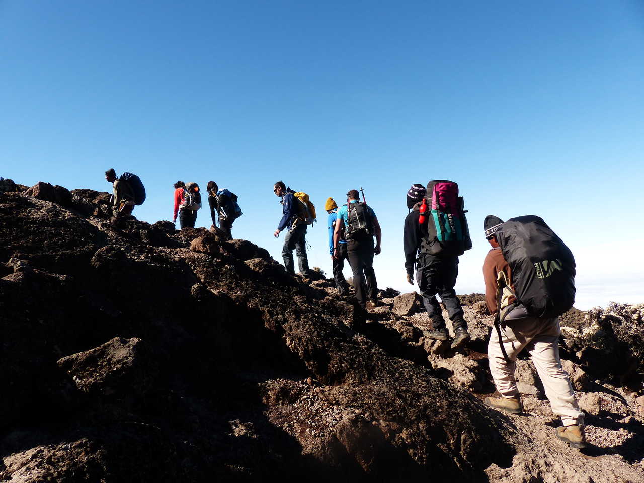 Petit groupe de randonneurs dans la montée dans le désert volcanique basaltique durant l'ascension du Kili Tanzanie