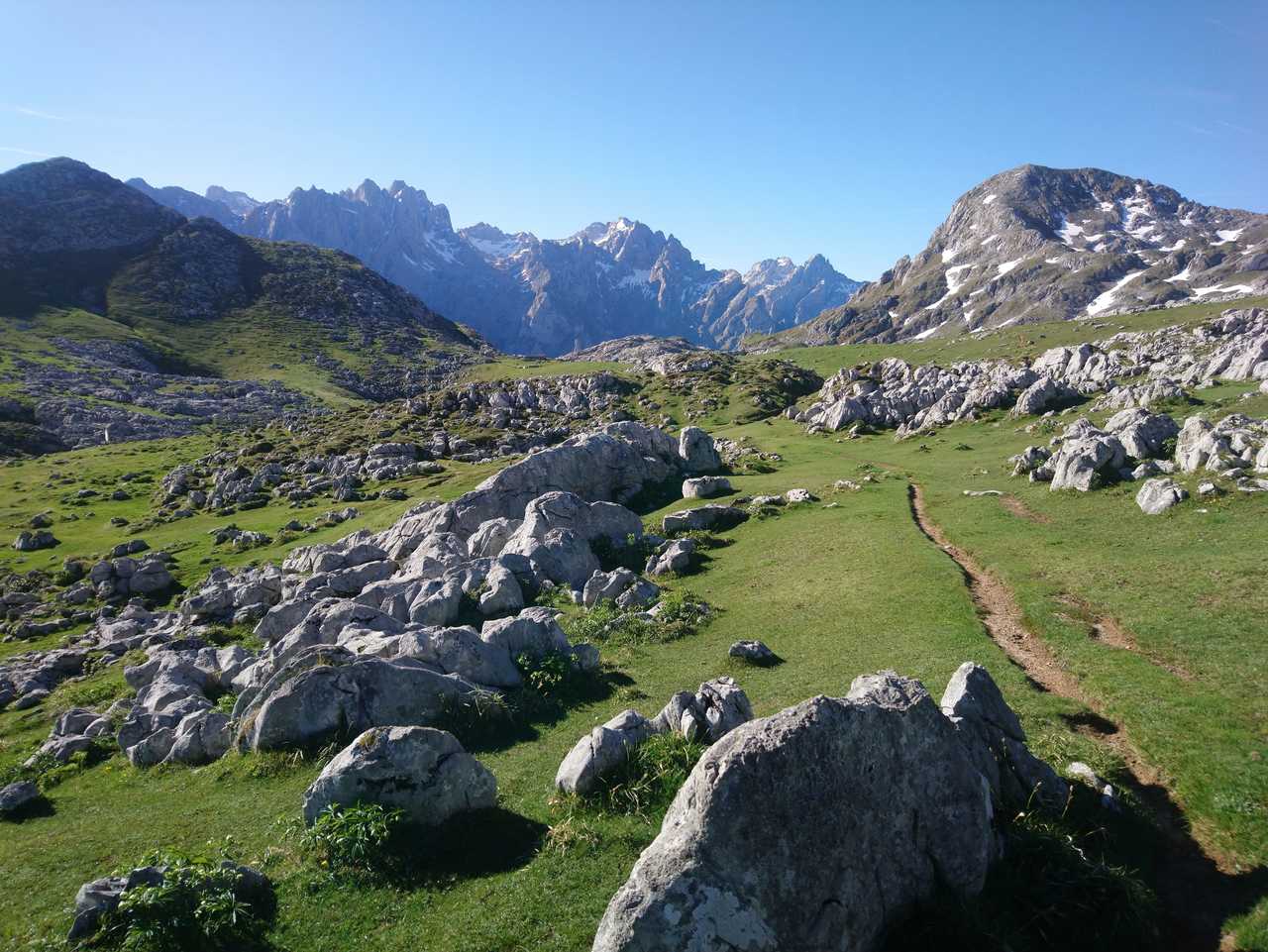 Sentier entre des étendues d'herbes vertes les sommets des Picos des Europa derrière