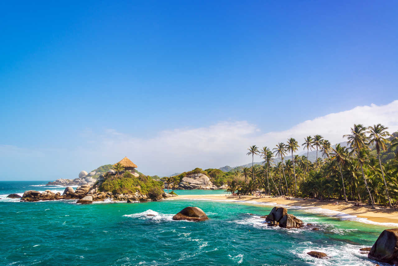 Plage de sable blanc bordée de cocotiers et d'énormes rochers de granit avec une mer turquoise cristalline dans le Parc National Tayrona.