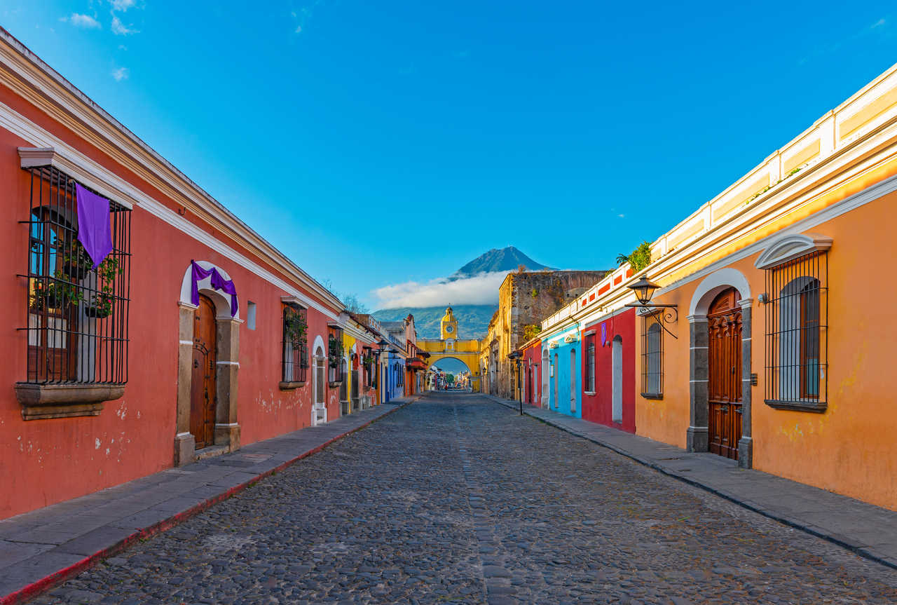 Rue pavée d'Antigua avec l'arche jaune emblématique et le cône parfait du volcan Agua en arrière-plan