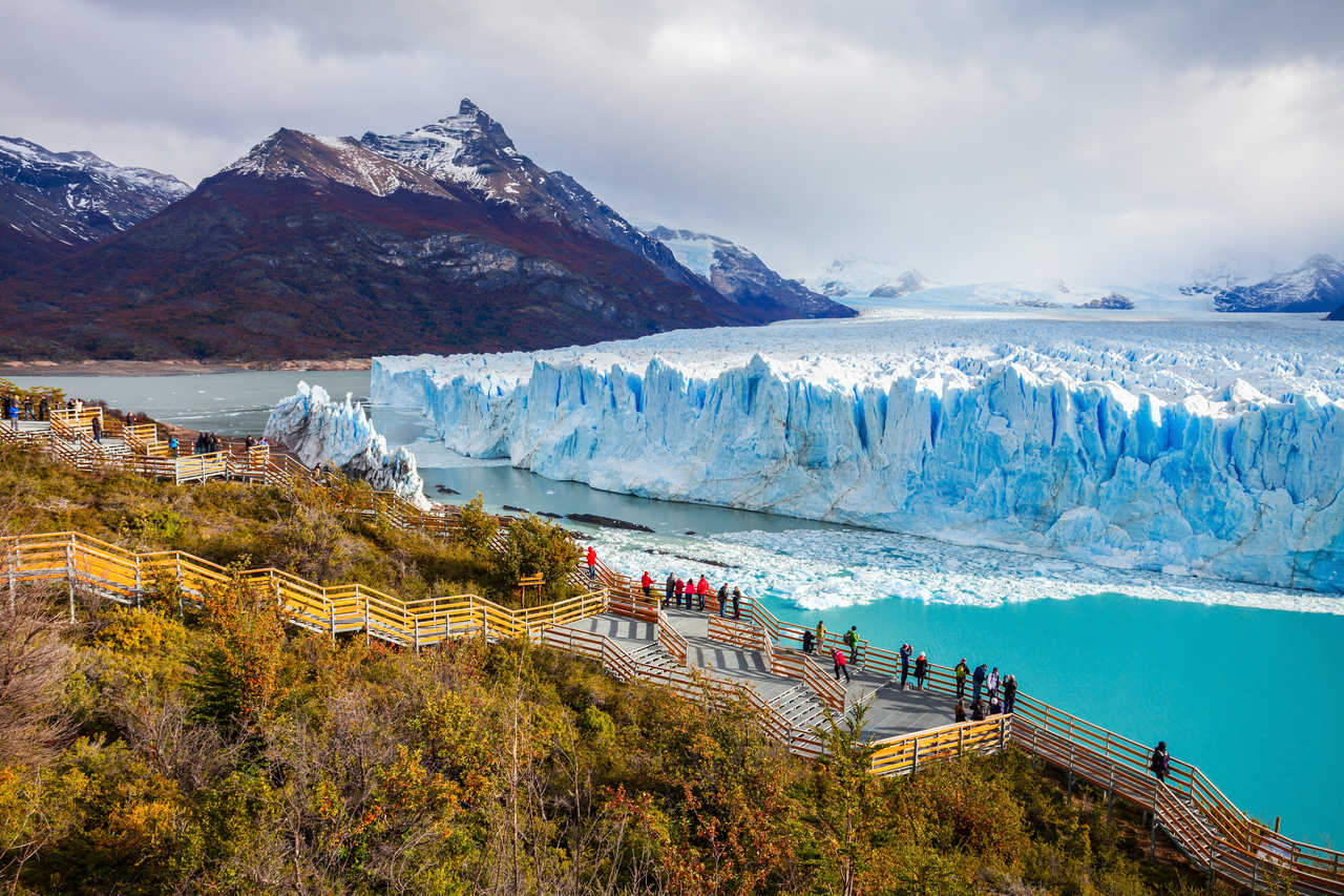 Voyageurs observant l'immense mur de glace bleue du glacier Perito Moreno depuis les passerelles en bois aménagées, dans le Parc National Los Glaciares en Patagonie argentine