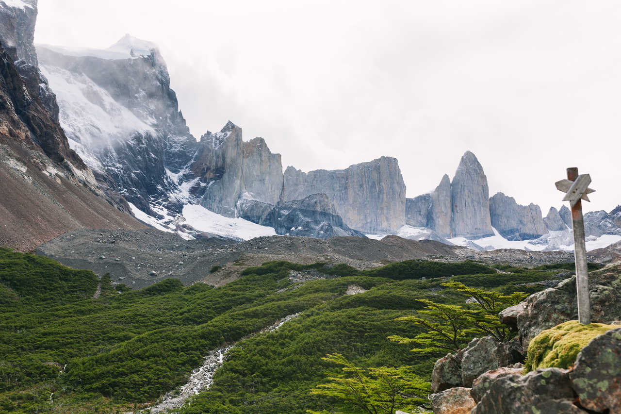 Vue spectaculaire sur l'amphithéâtre de granit et les sommets enneigés de la Vallée Frances, avec un panneau de randonnée en bois au premier plan, dans le parc national Torres del Paine au Chili.