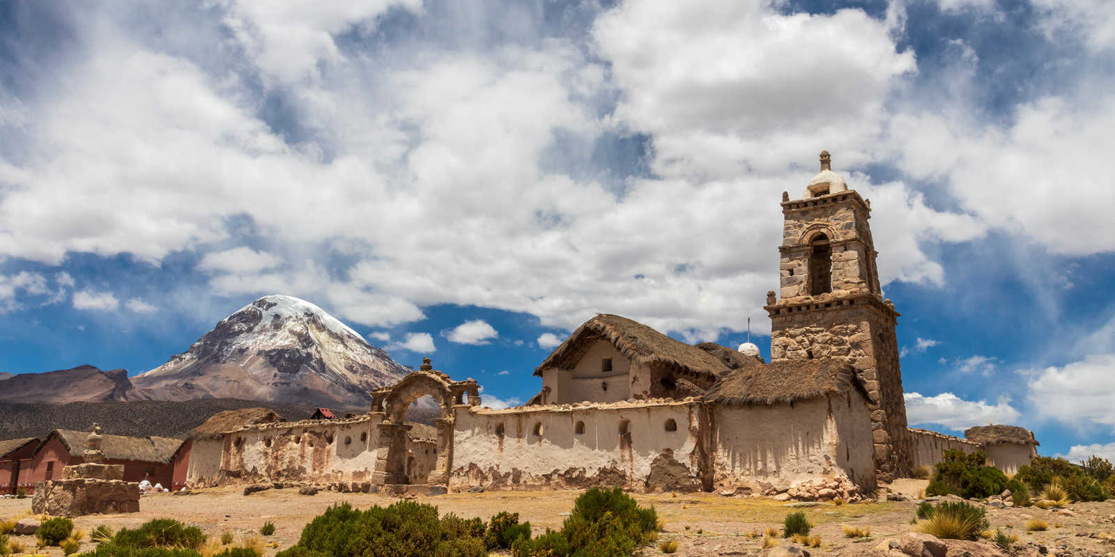 Vue sur une église en pierre au toit de chaume dans le village de Tomarapi avec le sommet enneigé du volcan en arrière plan © Jefwod