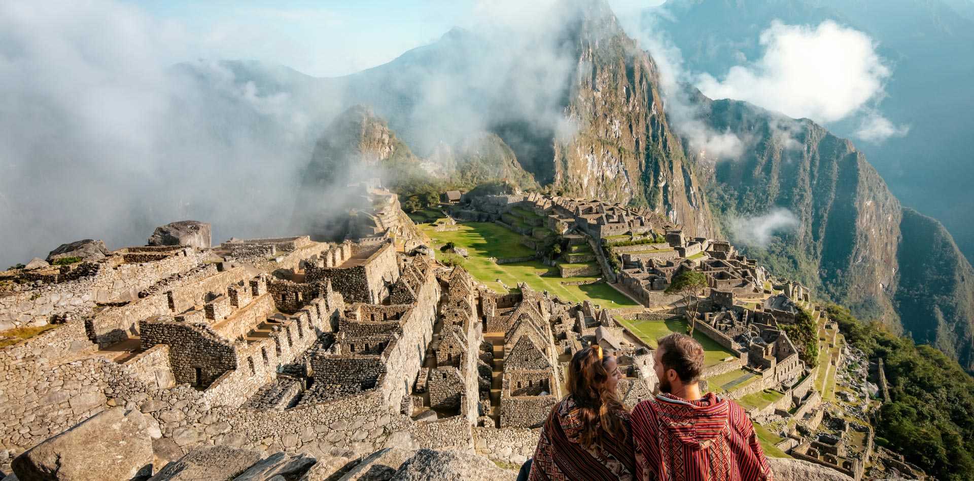 Couple voyageur face au Machu Picchu et ses nuages mystiques, au Pérou