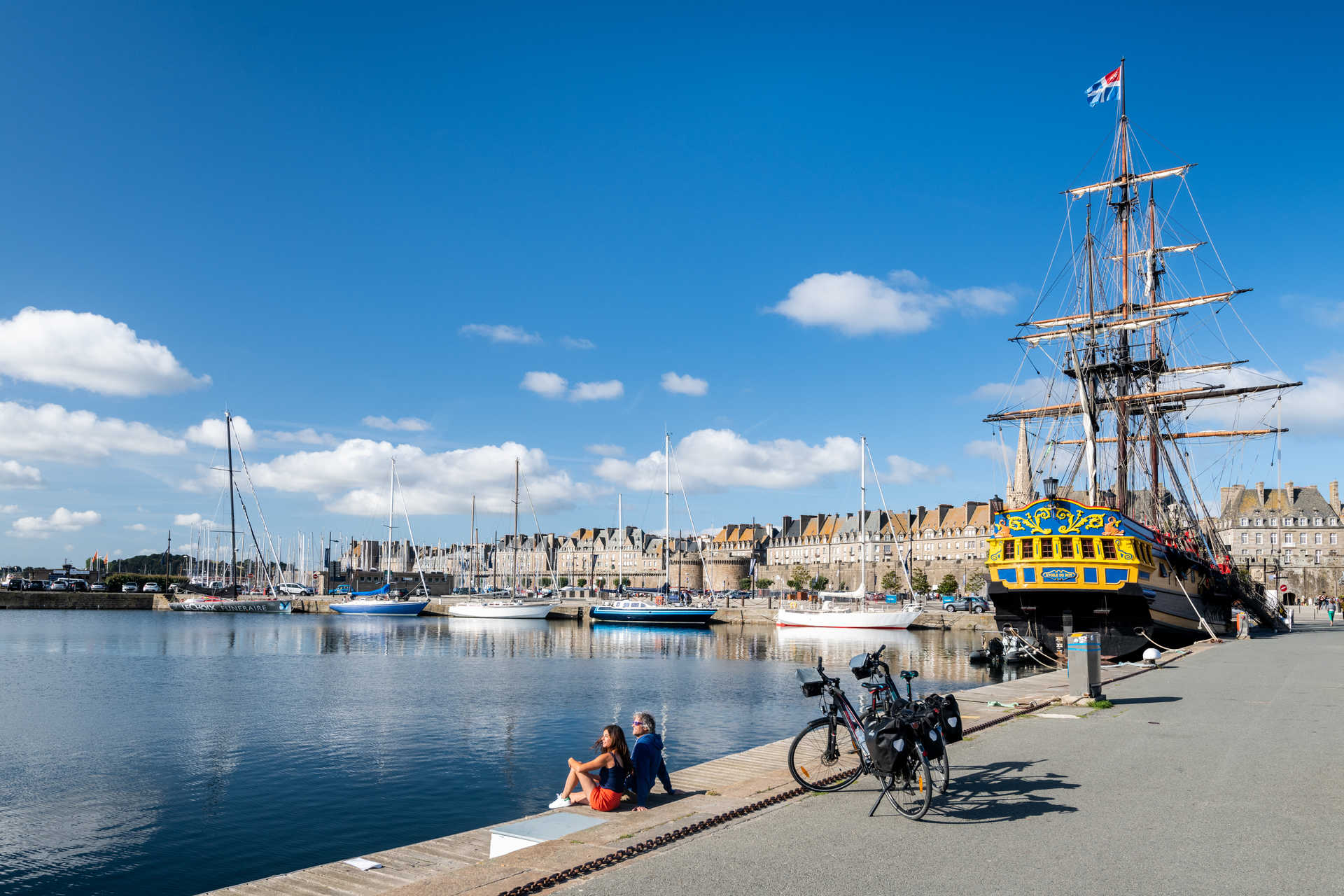 Cyclistes sur le port de Saint Malo avec le bateau l'étoile du roy en fond