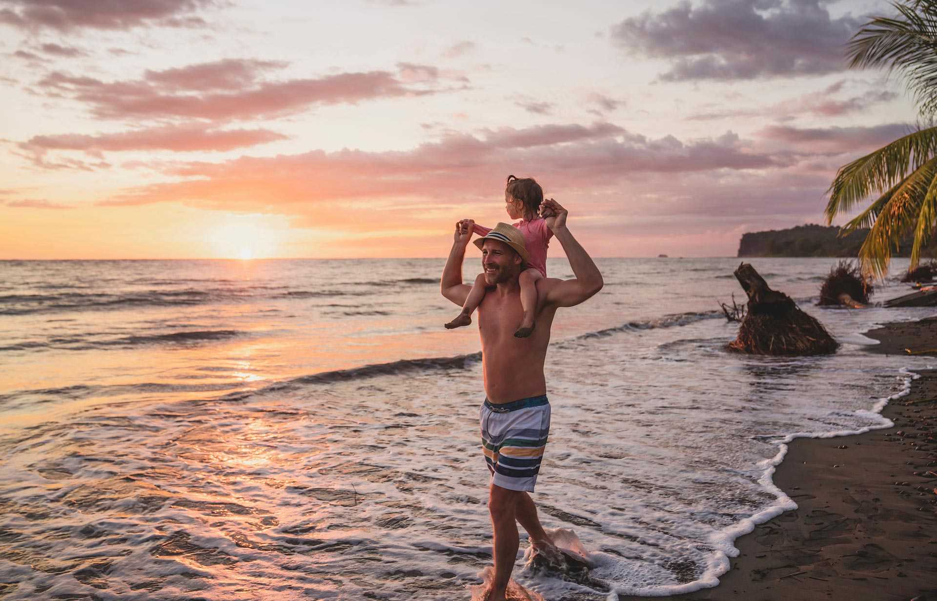 Père portant sa fille sur ses épaules, sur la plage du Costa Rica au coucher du soleil