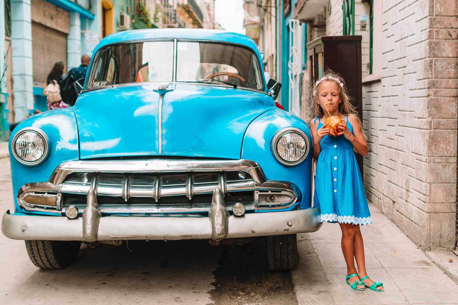 Petite fille buvant un jus de coco appuyée sur une vielle voiture américaine, à La Havane, à Cuba