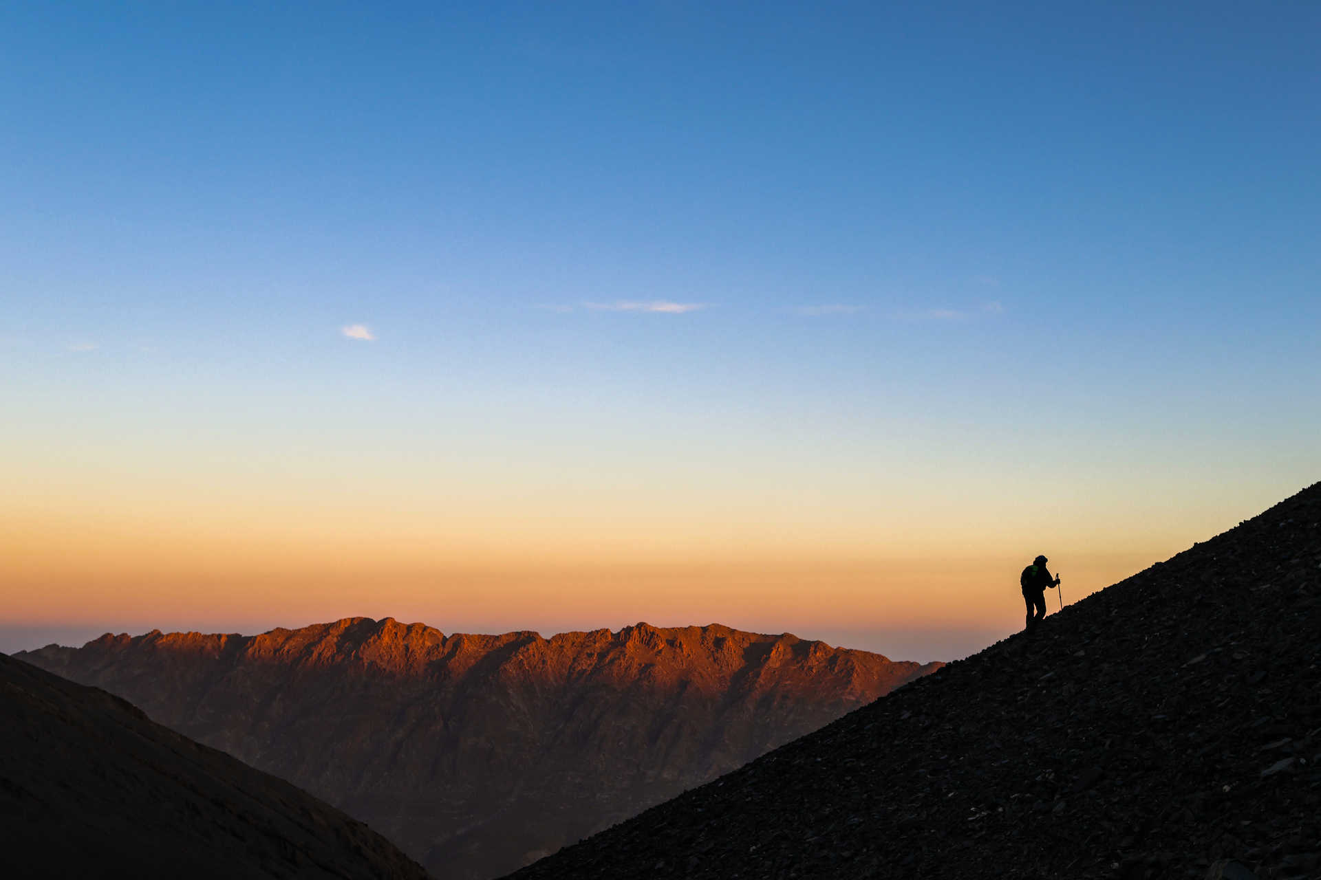 Silhouette d'un randonneur qui gravit une montagne au lever de soleil dans l'Atlas marocain au Maroc