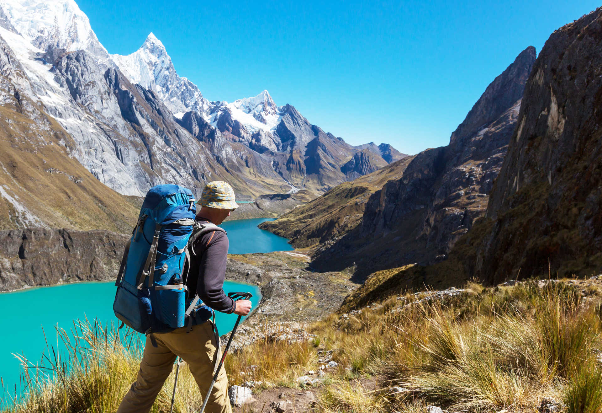 Un randonneur avec un sac à dos admire les trois lagunes glaciaires turquoise nichées au pied des sommets enneigés de la Cordillère Huayhuash