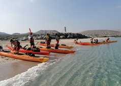 groupe de randonneurs qui se prépare à monter sur des kayaks sur une plage à Oman