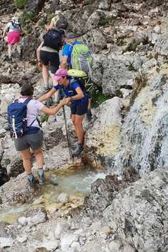 Aide de la guide au passage d'un ruisseau dans les Dolomites