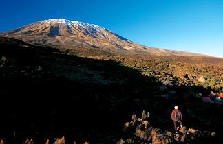 Un randonneur contemplant le massif du Kilimandjaro depuis un campement, en Tanzanie