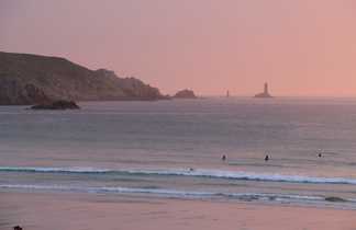 coucher de soleil sur une plage de surfeurs avec un phare en fond