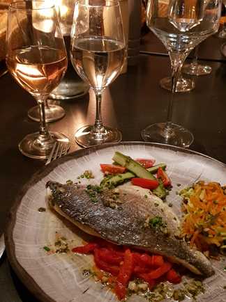 assiette avec poisson et vin blanc sur une table éclairée à l'aide d'une bougie