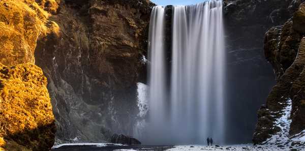 Couple de voyageurs devant la cascade de Skogafoss enneigée, en Islande