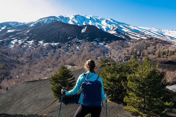 Randonneuse de dos face à l'Etna enneigé dans les forêts de pins au pied du volcan