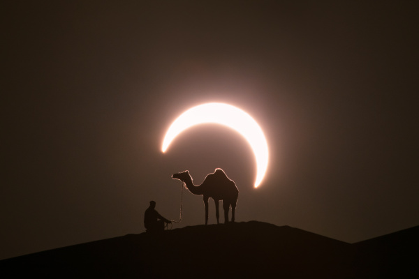 Silhouette d'un dromadaire et d'un homme sur une crête de dune de sable avec une éclipse solaire en arrière plan