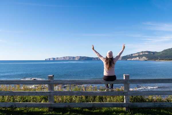 Voyageuse levant les bras devant un paysage de Gaspésie, au Canada