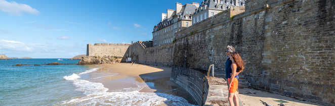 Cyclistes sur la plage de Saint-Malo avec les remparts et la ville intra-muros en fond