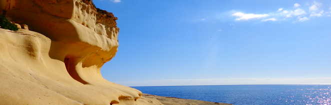 Falaise de calcaire érodé en une vague par le vent, le ciel bleu et la mer sont toujours présents