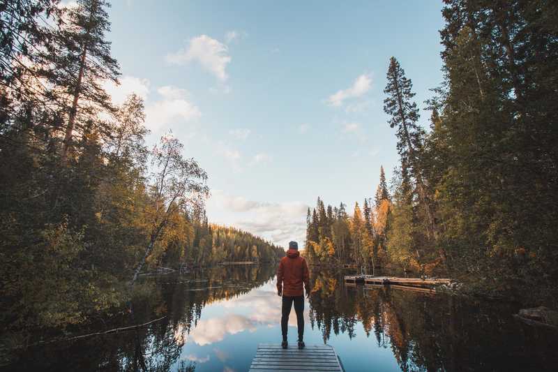 Randonneur face à un paysage de lacs et forêts en Finlande, l'été.